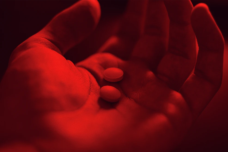 A red light cast over a hand holding two circular pills.