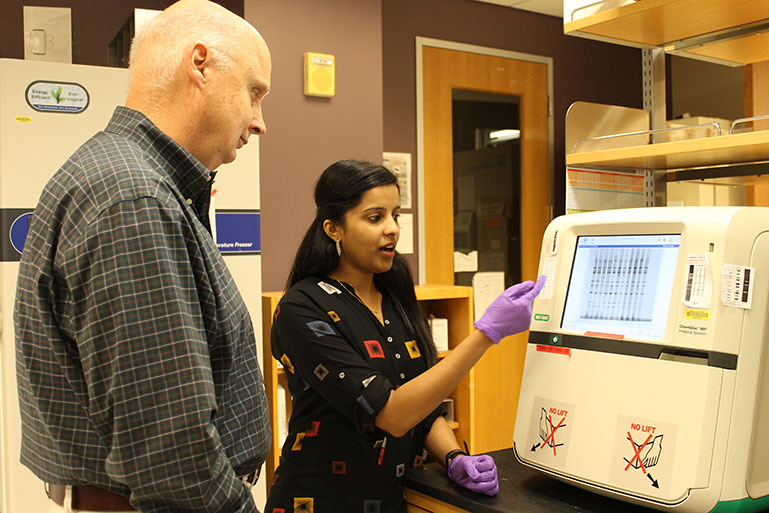John Patton and Asha Philip in a laboratory analyzing the results displayed on scientific equipment.
