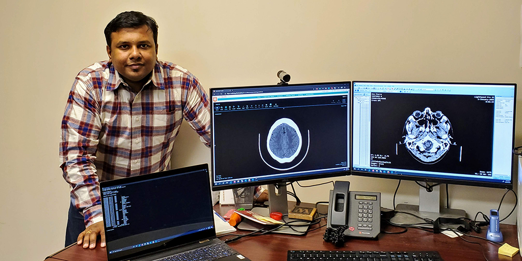 Saptarshi Purkayastha standing behind computer monitors displaying an image of a brain.
