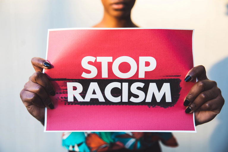 A woman with outstretched hands holding a sign saying 'STOP RACISM'.